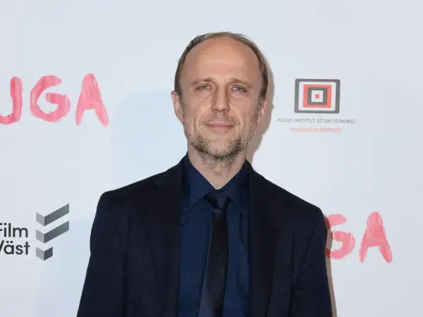 Łukasz Simlat, znany z wielu polskich filmów, na tle napisu "JUGA" i logo Polskiego Instytutu Sztuki Filmowej.