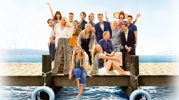 Obsada filmu "Mamma Mia!" na drewnianym molo z widokiem na morze.
