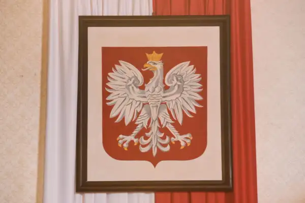 Orzeł Biały w koronie na czerwonej tarczy, symbol Polski. W tle biało-czerwone zasłony. Jakoś to będzie, nawet w trudnych czasach.